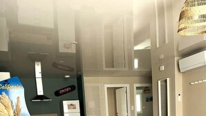 Un saló modern amb un sofà, una taula de menjador, cadires, un seient de bossa i una cuina al fons.