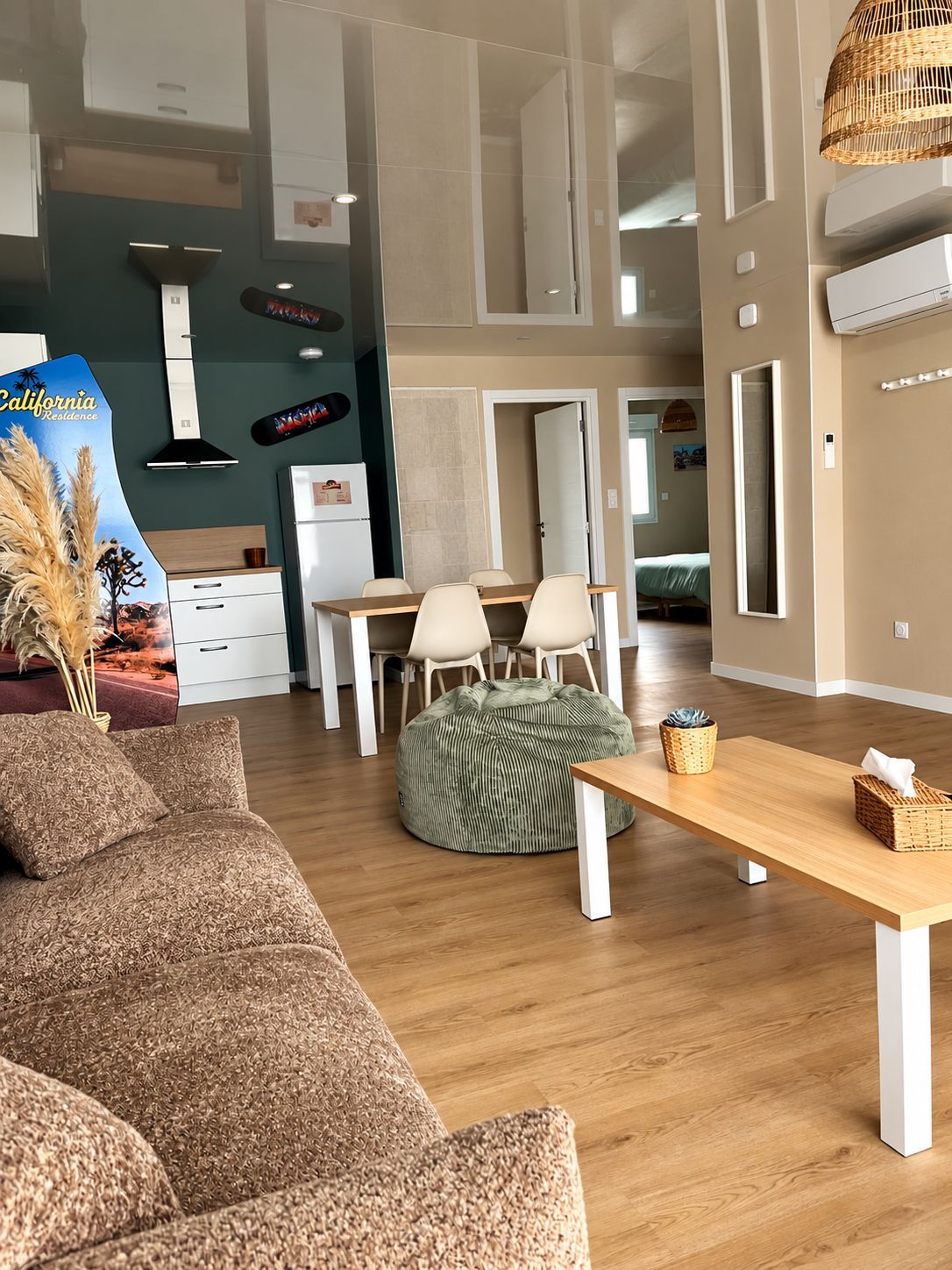 Ein modernes Wohnzimmer mit einer Couch, einem Esstisch mit Stühlen, einem Sitzsack und einer Küchenzeile im Hintergrund.