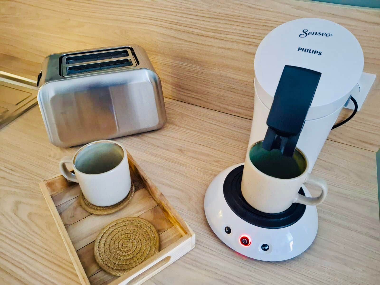 Una macchina da caffè, un tostapane e un vassoio con una tazza e un sottobicchiere su un piano di legno.