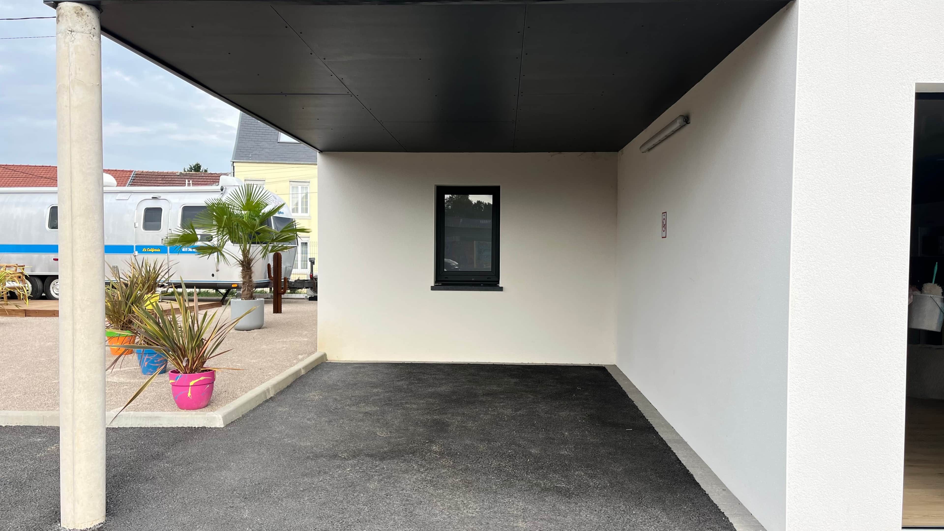 A covered outdoor area with a concrete floor, a small window, and potted plants.
