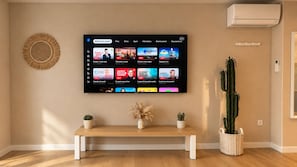 A living room with a flat-screen TV mounted on the wall displaying a streaming service interface. - San Francisco - Apartment in a complex with a pool (Neuf-Mesnil)