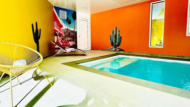 Zona d'una piscina interior moderna, amb una combinació de groc i taronja, una piscina, gandules i una decoració de cactus.