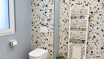 A bathroom with a white toilet, a wall-mounted towel rack, and a trash bin.