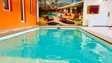 Una piscina con un mural de paisaje tropical, paredes anaranjadas y sillas amarillas.