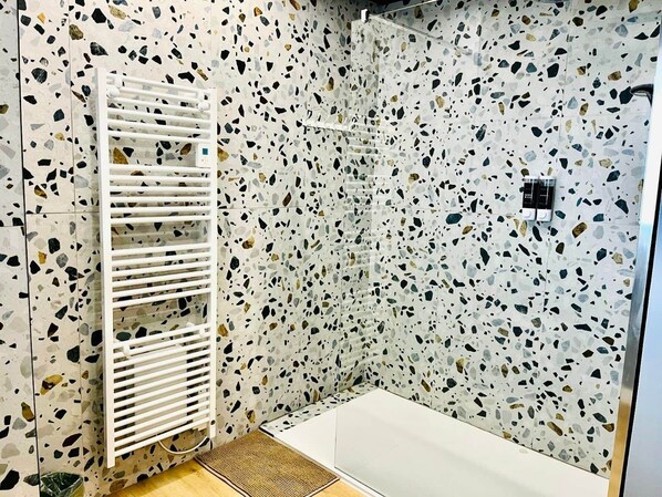 A bathroom with a terrazzo floor, a white shower enclosure, and a white towel rack.