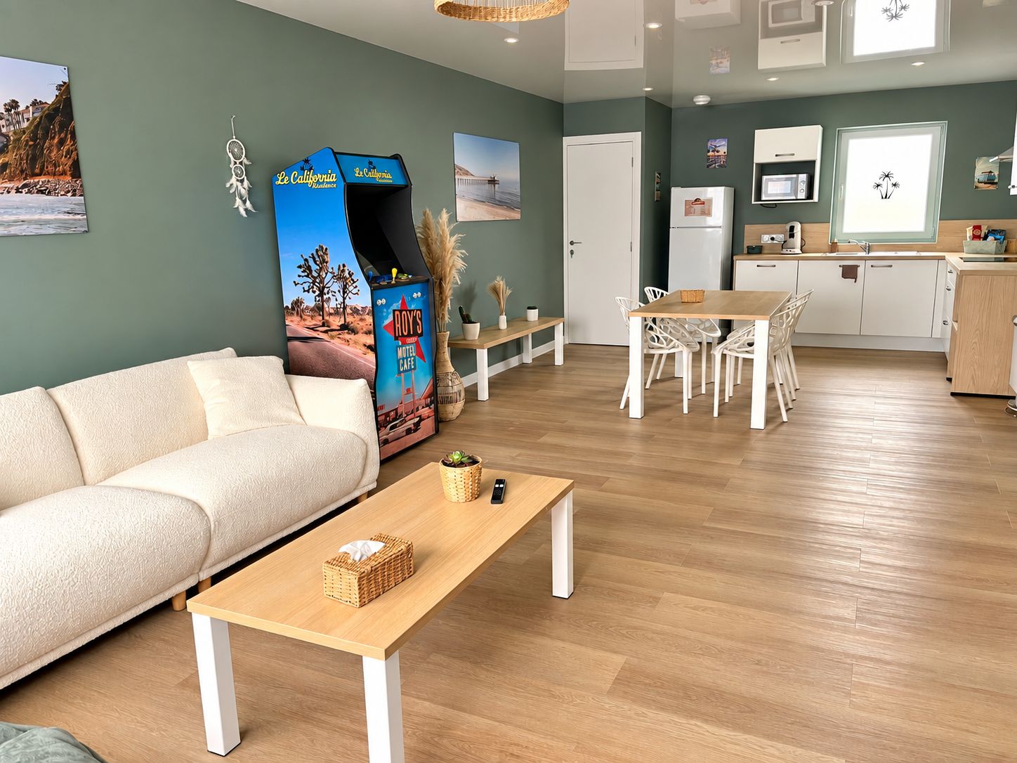 A modern living room with a sofa, a coffee table, and a dining area with chairs. There is a kitchen area with a refrigerator and a microwave.