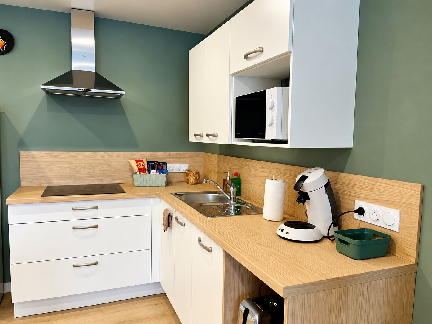 Een moderne keuken met een roestvrijstalen afzuigkap, witte kasten, een magnetron en een koffieapparaat.