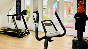 Un gimnasio moderno con dos cintas de correr, una elíptica y una bicicleta estática. Amplias ventanas ofrecen luz natural y vistas al exterior.