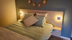 Una cama bien hecha con cabecera, dos lámparas de pared y tres adornos circulares en la pared.