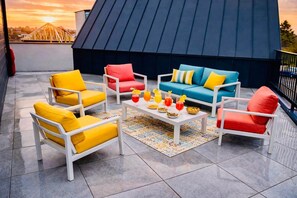 A rooftop patio with white furniture, a coffee table with drinks, and a view of a bridge.