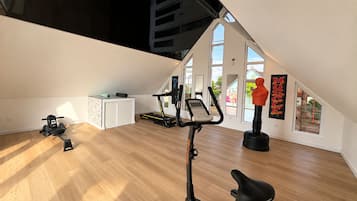 Ein geräumiges Zimmer mit Deckenventilator, Laufband, Heimtrainer und Yogamatte.