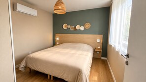 A bedroom with a bed, bedside tables, wall-mounted air conditioning, a hanging light fixture, and decorative wall art. - Venice Beach - Apartment in a complex with a pool (Neuf-Mesnil)