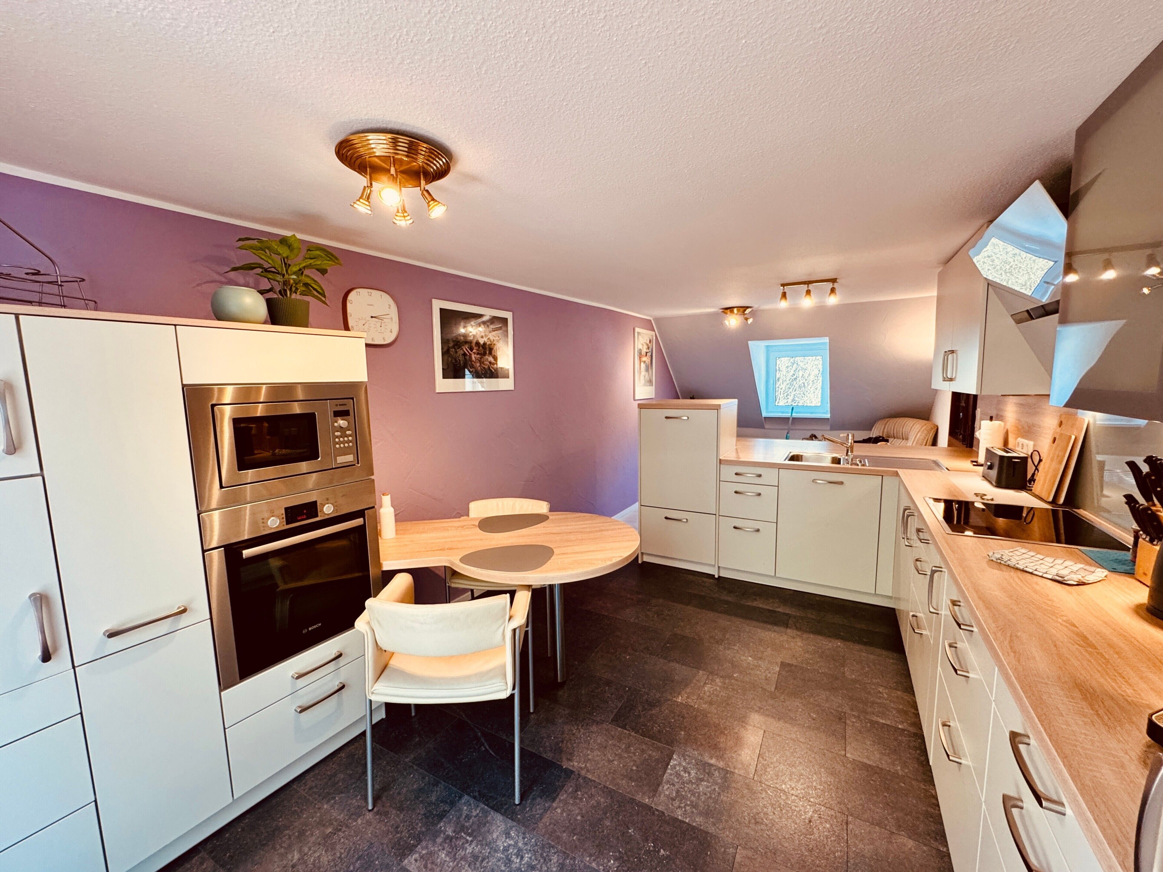 A modern kitchen with a round dining table, built-in oven, and a window with a view.