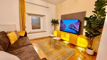 Un salon avec un canapé, un téléviseur, une fenêtre, une plante et un meuble jaune.