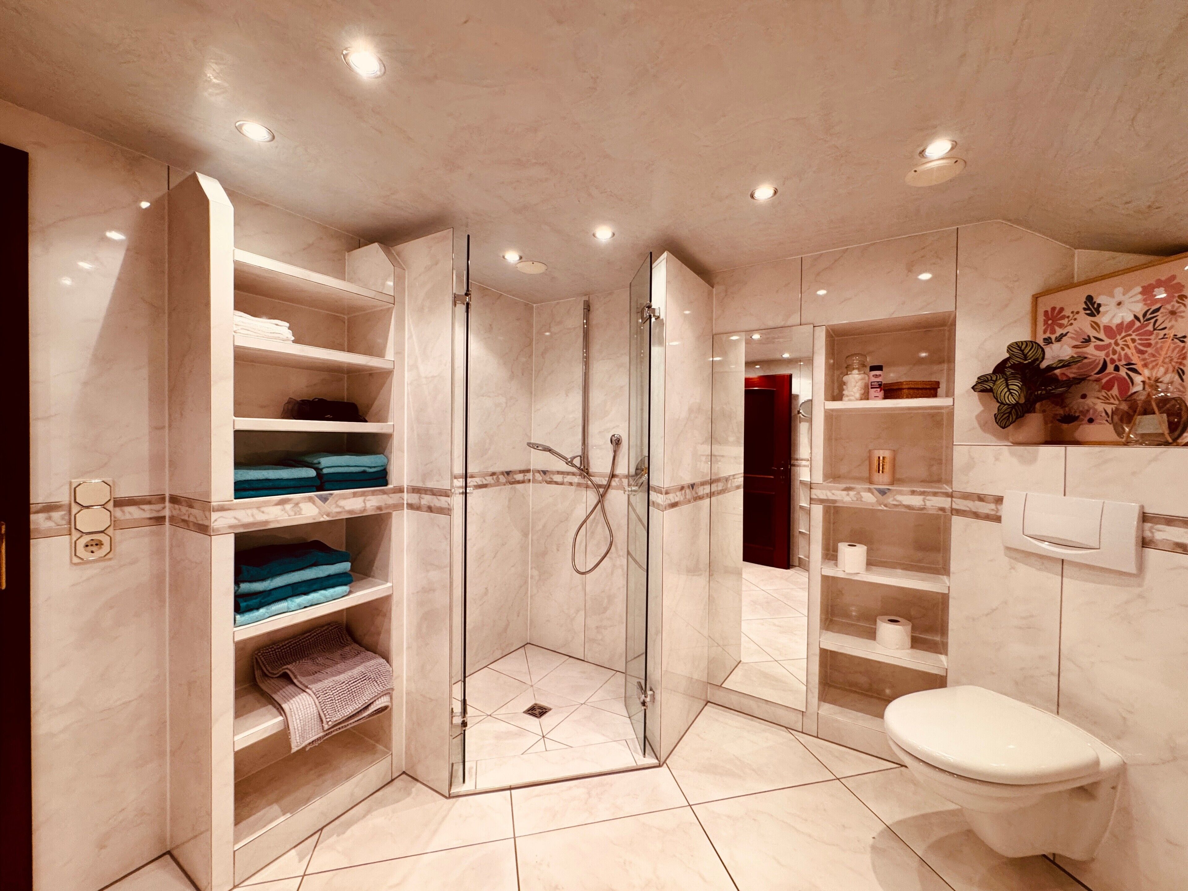 Ein modernes Badezimmer mit einer Glaskabine zur Dusche, Marmorregalen und einer Toilette.