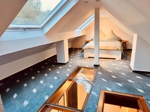 A bedroom with a skylight, a bed, a bedside table, and a small stool.