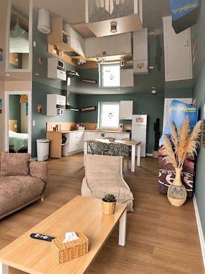 Un espai habitable compacte amb petita cuina, zona de menjador i saló amb sofà i taula.
