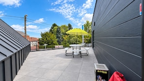 Patio esterno con tavolo e sedie, un ombrellone giallo e un cestino.