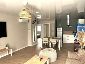 A modern living room with a dining area, a kitchen, and a large window. - Laguna Beach - Suite in residence with swimming pool (Neuf-Mesnil)