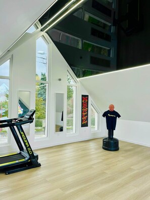 A modern room with a treadmill, a punching bag, and large windows offering a view of the outdoors. - ⭐ Hollywood Suite - Suite in residence with swimming pool (Neuf-Mesnil)