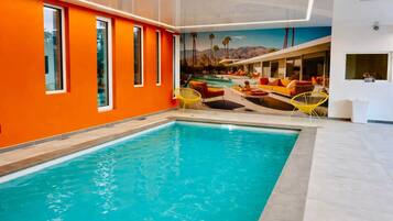 Piscina interior con paredes naranjas y un mural de paisaje tropical.