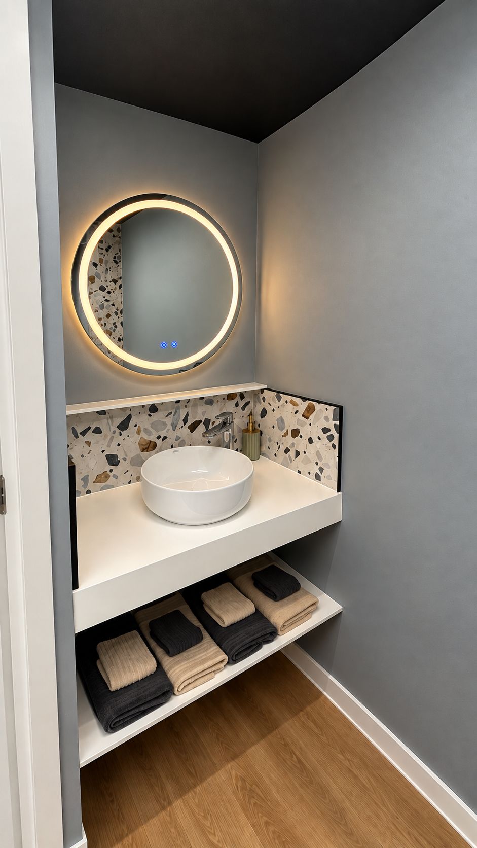 Une salle de bain avec un miroir rond, un lavabo blanc et une étagère où sont pliées des serviettes.