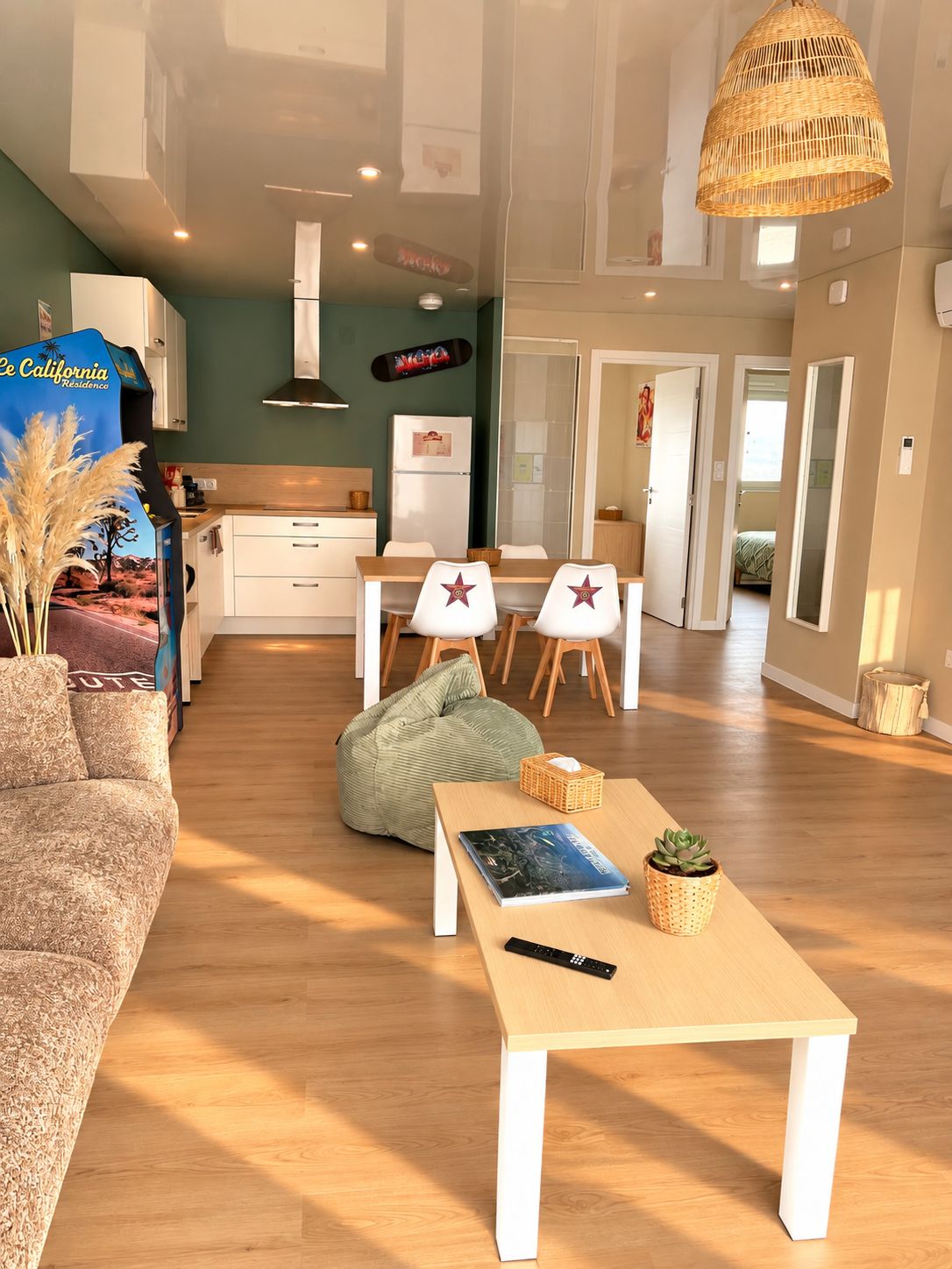 Een moderne woonkamer met een bank, een bijzettafeltje met een boek en afstandsbediening, een groene relaxstoel en een eethoek met stoelen en een tafel.