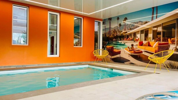 An indoor swimming pool with a mural of a mountain landscape, orange walls, and yellow chairs. - Palm Springs - Family suite with pool (Neuf-Mesnil)