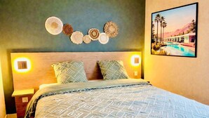 A bed with a patterned bedspread, two pillows, a headboard, bedside lamps, and a wall-mounted decorative item. - Palm Springs - Family suite with pool (Neuf-Mesnil)