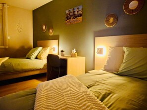 A room with two beds, a desk, and a chair. There are wall-mounted lights and a poster on the wall.