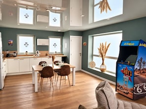 A modern kitchen with white cabinets, a dining area with brown chairs, and a large window with a view of the sky.