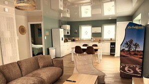 A modern living room with a sofa, a coffee table, and a dining area with chairs. - Palm Springs - Family suite with pool (Neuf-Mesnil)