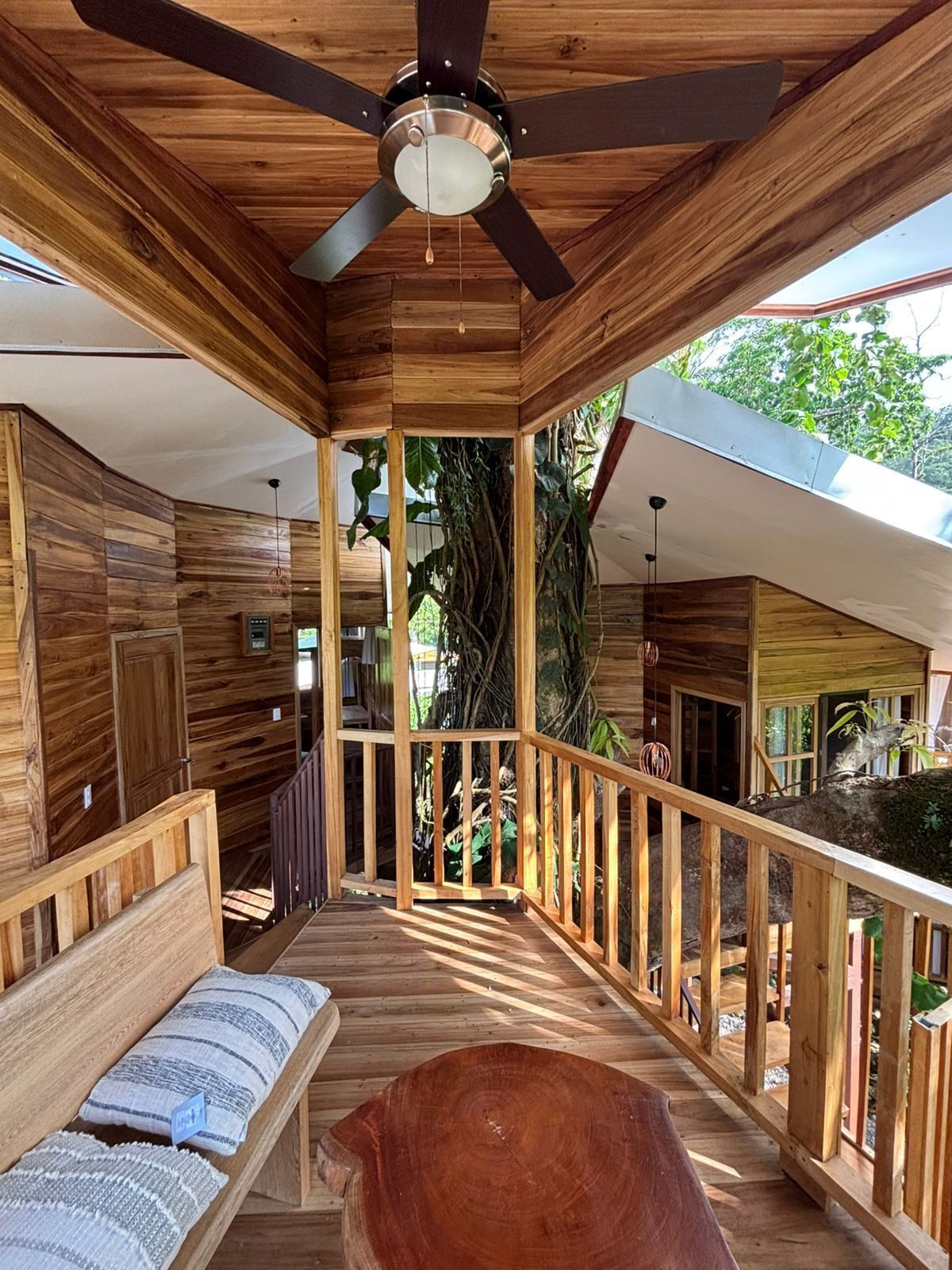 Eine Holzdielen-Terrasse mit Deckenventilator, einer Bank mit Kissen und einer Geländer.