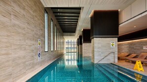 Una piscina con pavimento piastrellato, tetto apribile e area relax con lettini.