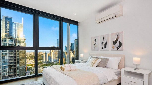 Una camera da letto moderna con un letto grande, un comodino, e vista sulla città attraverso ampie finestre.