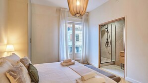 Una camera d'albergo con un letto, un bagno con doccia, una finestra con tende e un lampadario.