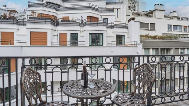 Un balcone con un tavolo rotondo, sedie, una bottiglia di vino e un bicchiere.