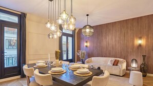 Un'area pranzo con un tavolo grande apparecchiato per sei persone, circondato da sedie, con lampadari sospesi sopra.