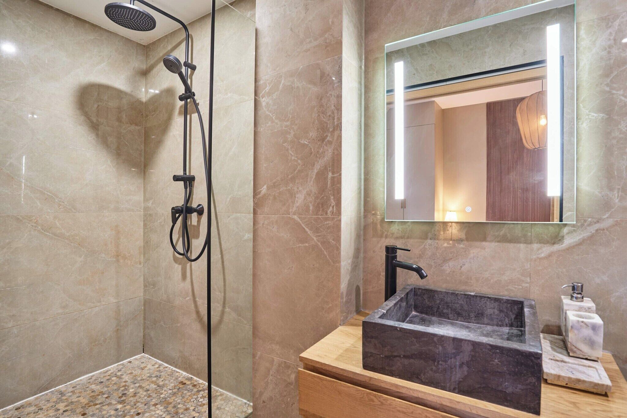 A bathroom with a shower, a sink with a marble basin, and a mirror with a light above it.