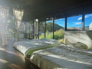 Una habitación con dos camas, amplias ventanas y vistas a zonas verdes.