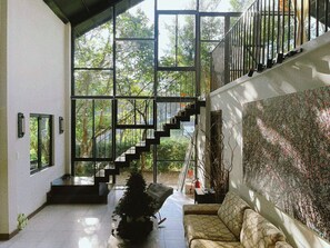Ein großzügiger Innenraum mit einer Treppe zu einem Balkon, großen Fenstern und einem an der Wand befestigten Kunstwerk.