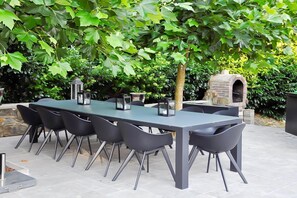 An outdoor dining area with a long table and chairs, surrounded by lush greenery. - Luxury Ardennes Villa with Pool and Sauna (Stoumont)