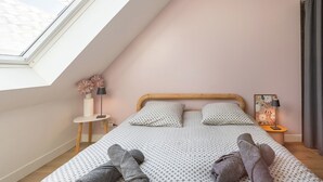 A bedroom with a sloped ceiling, a bed with patterned bedding, a bedside table with a lamp, and a window with a view. - Ty Elise – Charming Central Apartment in the Heart of Quimper (Quimper)