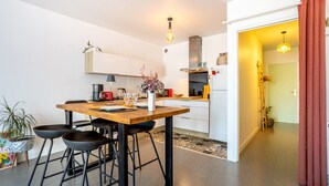A modern kitchen with a wooden table, black bar stools, and a hanging light fixture. - Ty Elise – Charming Central Apartment in the Heart of Quimper (Quimper)