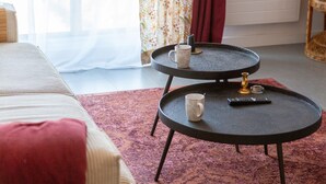 A room with a bed, a round black table with a remote control and a mug, and a patterned curtain. - Ty Elise – Charming Central Apartment in the Heart of Quimper (Quimper)