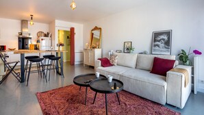 A modern living room with a sofa, coffee table, and a kitchen area in the background. - Ty Elise – Charming Central Apartment in the Heart of Quimper (Quimper)