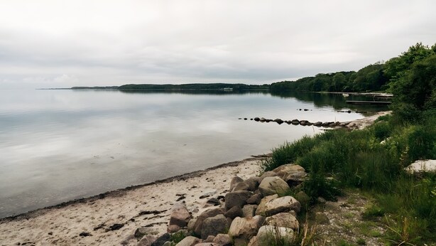 A calm lake with a sandy beach and a stone wall.