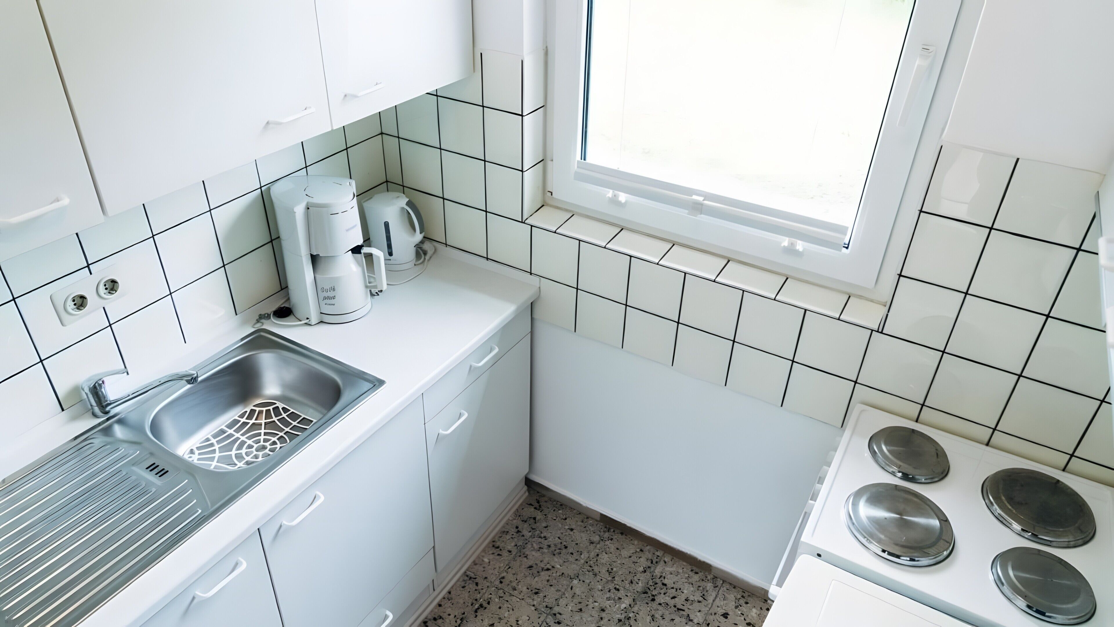 Een keuken met witte kastjes, een roestvrijstalen spoelbak, een koffiezetapparaat en een fornuis.