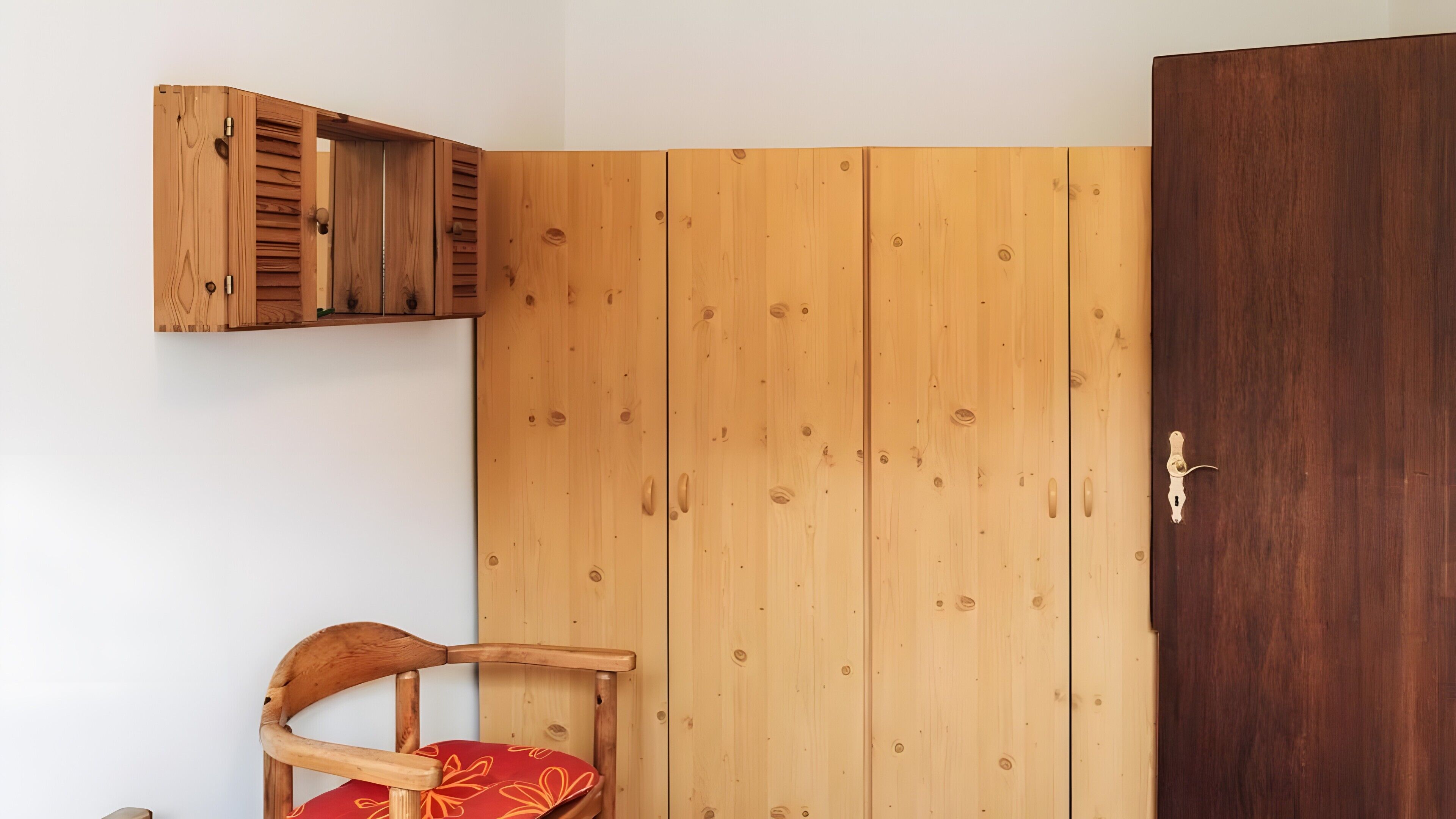 Een kamer met een houten garderobe, een houten stoel met een rode kussen en een houten kast.