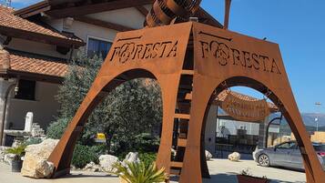 Un arco de metal con 'FORESTA' escrito, que da paso a un edificio de tejado a la vista.